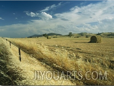 A Hay Field with Bales Sitting under a Cloud Filled Sky