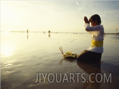 A Kneeling Hindu Balinese Woman Prays and Gives Offerings at Sunset
